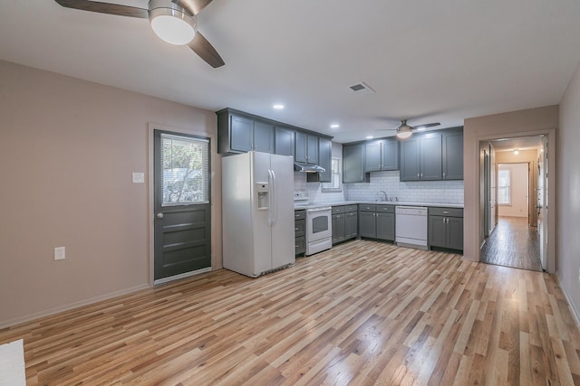 kitchen with under cabinet range hood, white appliances, visible vents, light wood finished floors, and tasteful backsplash