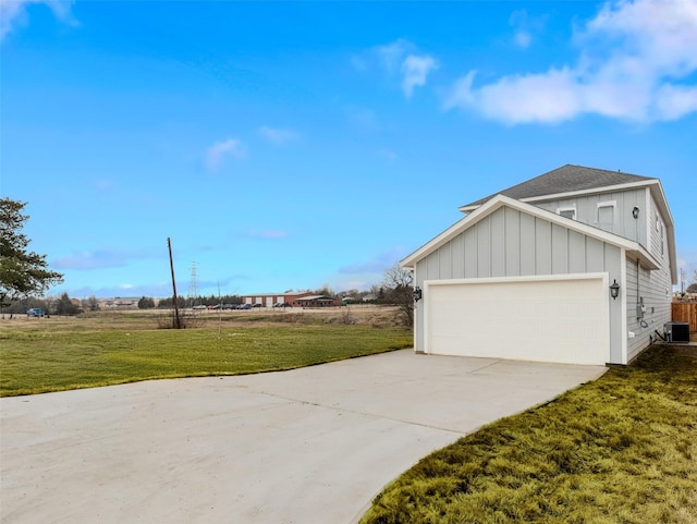 view of side of home with an attached garage, central AC, a yard, concrete driveway, and board and batten siding