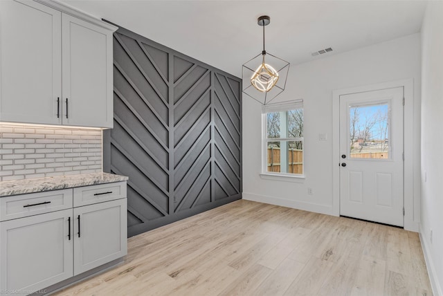 unfurnished dining area featuring light wood-style flooring, visible vents, and baseboards