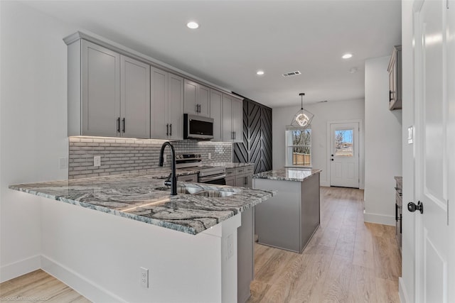 kitchen with visible vents, appliances with stainless steel finishes, light stone counters, a center island, and gray cabinets