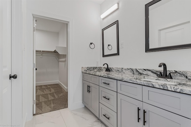 bathroom with a walk in closet, marble finish floor, double vanity, a sink, and baseboards