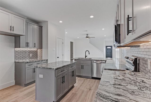 kitchen with gray cabinetry, a sink, light wood-style floors, appliances with stainless steel finishes, and light stone countertops