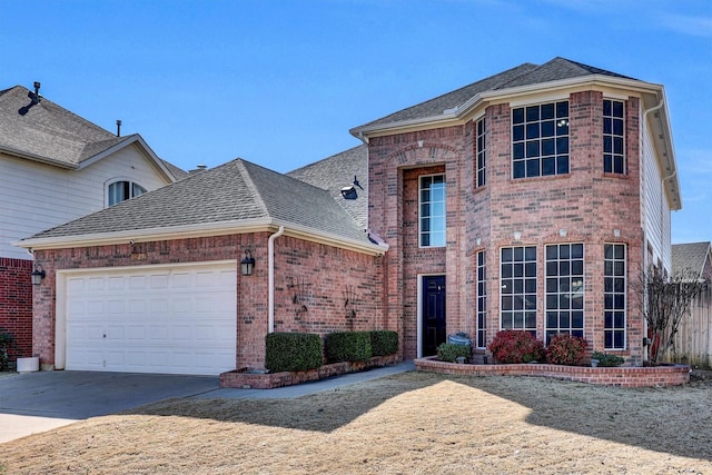 traditional-style home featuring a garage, a shingled roof, concrete driveway, and brick siding