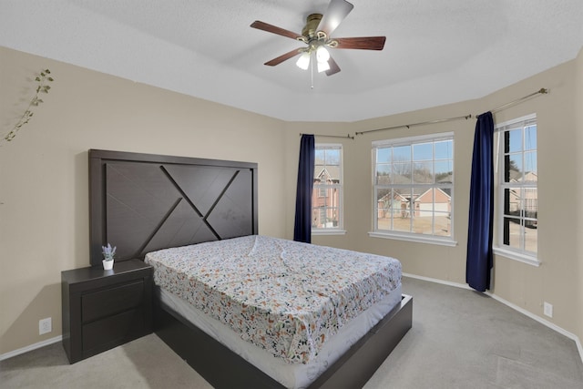 carpeted bedroom with a tray ceiling, ceiling fan, and baseboards