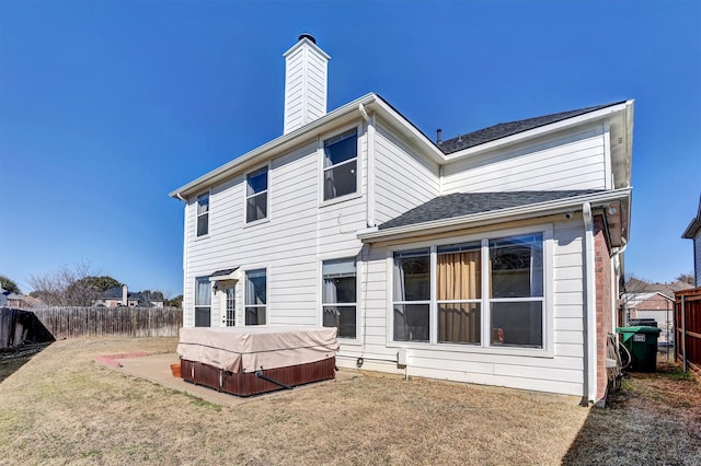 back of property with a hot tub, a chimney, fence, and a yard