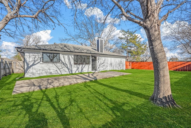 back of house featuring a yard, a shingled roof, a chimney, and a fenced backyard