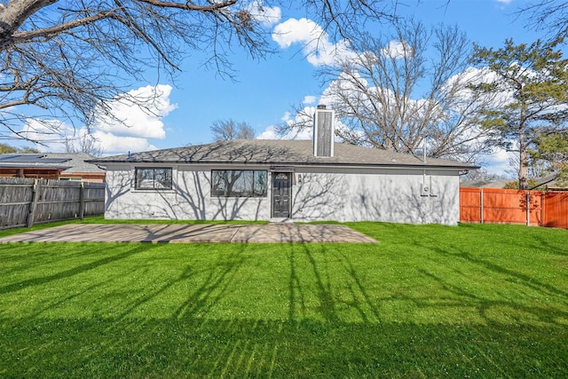 rear view of house featuring a fenced backyard, a yard, and a chimney