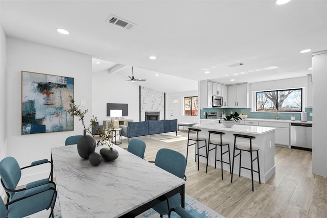 dining space with lofted ceiling with beams, a premium fireplace, visible vents, a ceiling fan, and light wood-type flooring