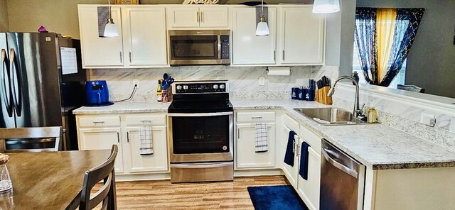 kitchen with white cabinets, a sink, decorative backsplash, light wood-style flooring, and appliances with stainless steel finishes