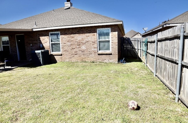 rear view of house with a fenced backyard, brick siding, a shingled roof, a yard, and a chimney