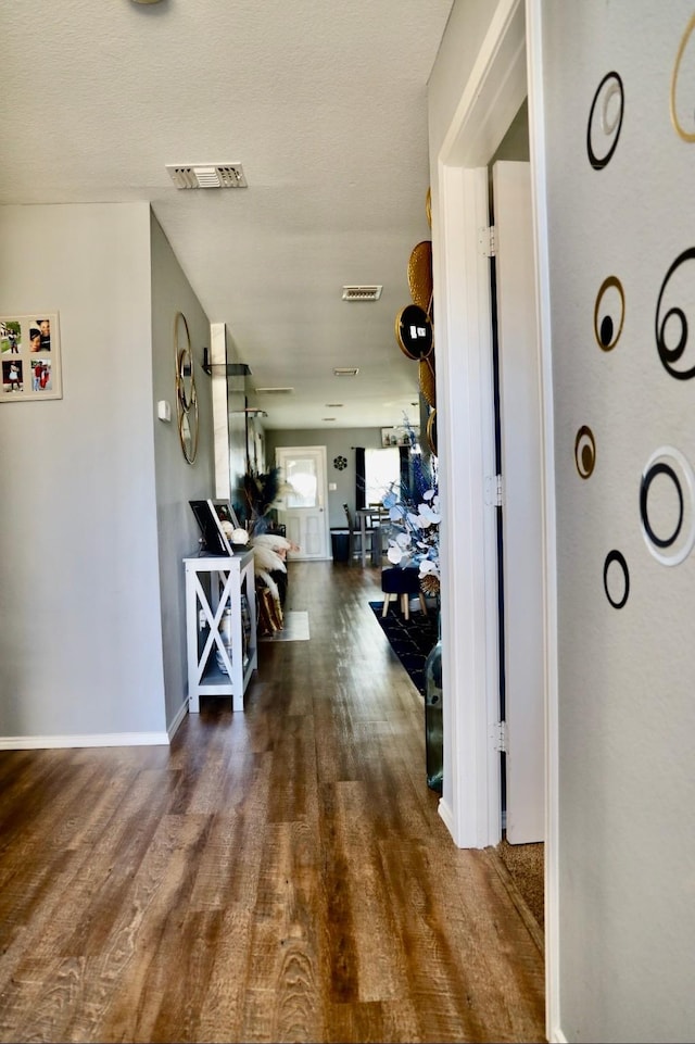 hallway featuring visible vents, baseboards, and wood finished floors