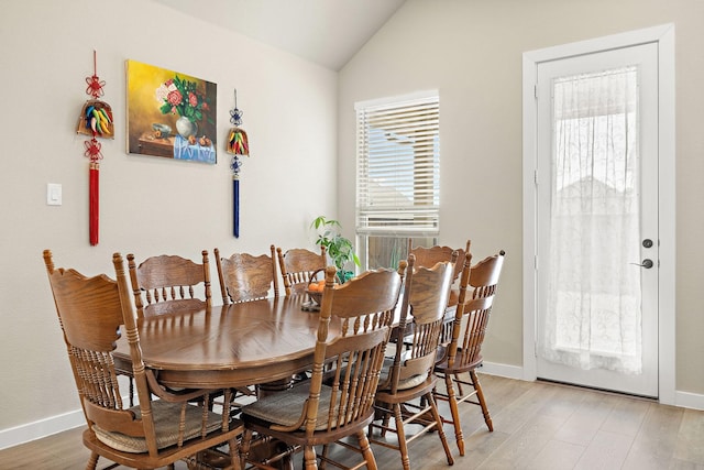 dining room with light wood-type flooring, a wealth of natural light, vaulted ceiling, and baseboards