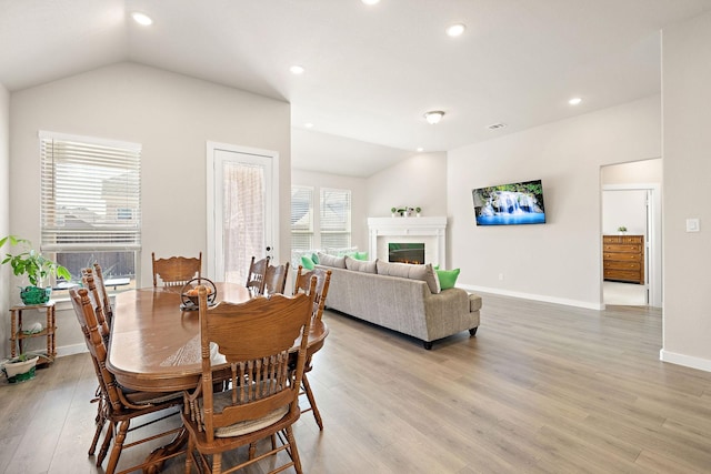 dining room with a warm lit fireplace, recessed lighting, baseboards, vaulted ceiling, and light wood finished floors