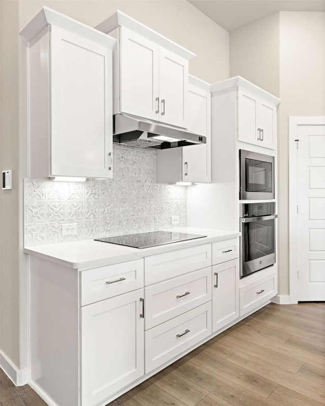 kitchen with oven, built in microwave, black electric cooktop, light countertops, and under cabinet range hood