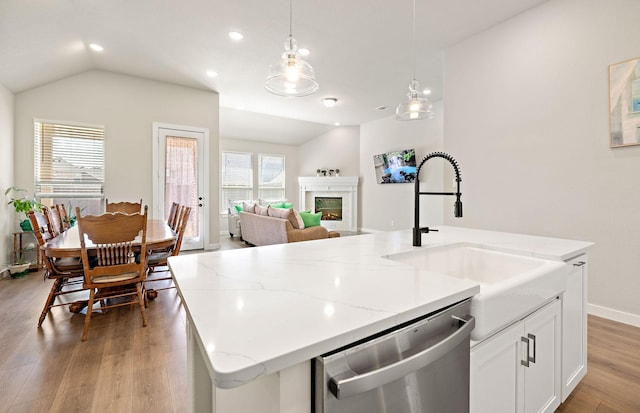 kitchen featuring dishwasher, a glass covered fireplace, lofted ceiling, wood finished floors, and a kitchen island with sink