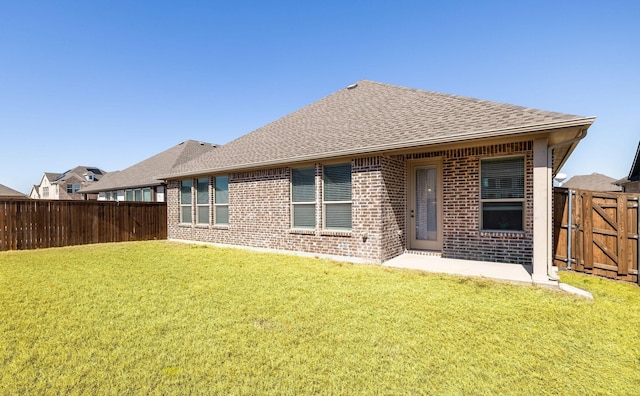 rear view of house with brick siding, roof with shingles, a fenced backyard, and a yard