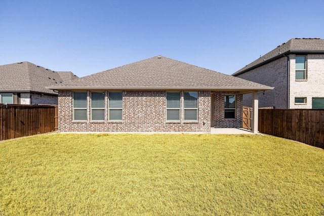 rear view of house with roof with shingles, brick siding, a lawn, and a fenced backyard