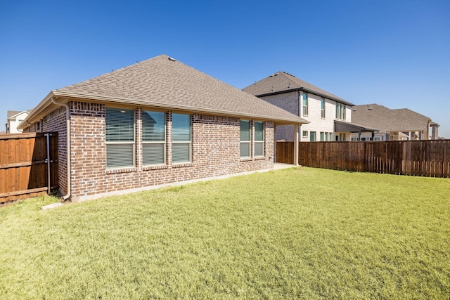 back of property featuring brick siding, a lawn, a shingled roof, and a fenced backyard