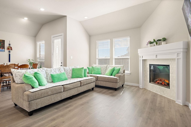 living area with lofted ceiling, recessed lighting, light wood-style flooring, a glass covered fireplace, and baseboards