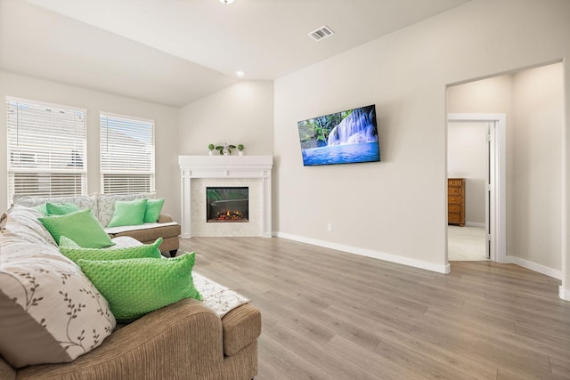 living room with light wood finished floors, baseboards, visible vents, a glass covered fireplace, and vaulted ceiling