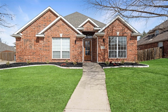 view of front facade with a front yard, brick siding, fence, and roof with shingles