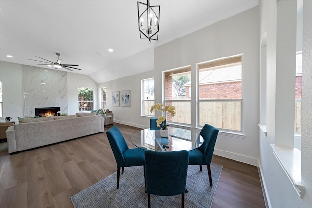 dining room with a premium fireplace, baseboards, vaulted ceiling, and wood finished floors