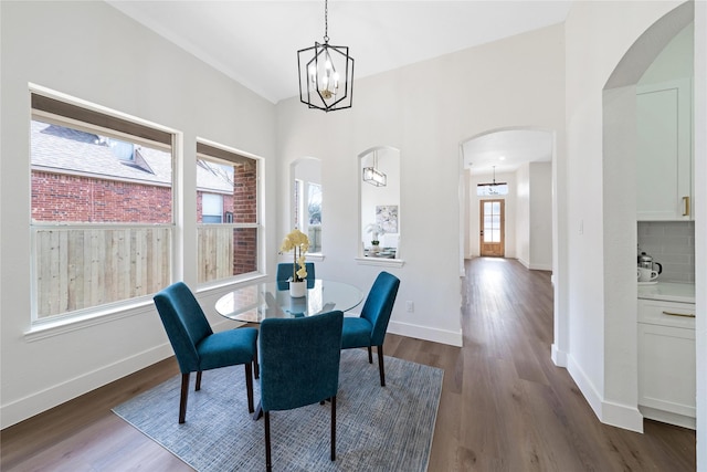 dining area with baseboards, a notable chandelier, arched walkways, and dark wood-style flooring