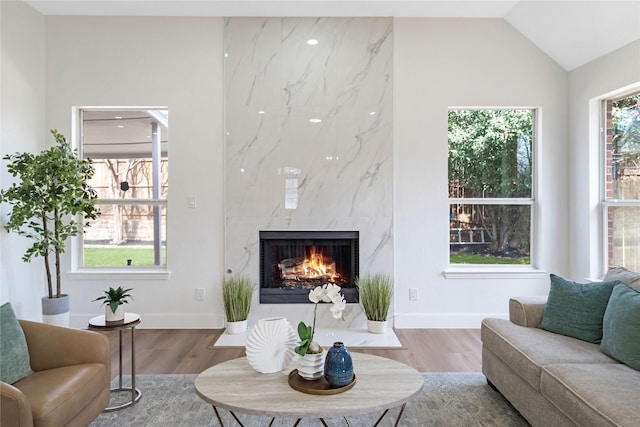 living area with a premium fireplace, baseboards, vaulted ceiling, and wood finished floors