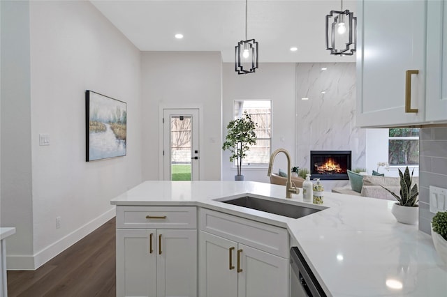 kitchen featuring dark wood-style floors, hanging light fixtures, a premium fireplace, white cabinets, and a sink