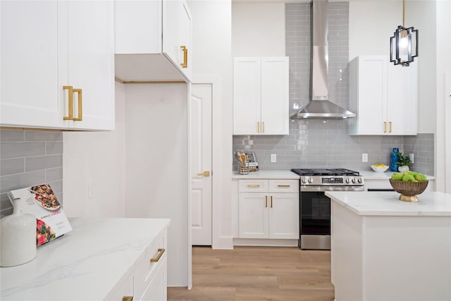 kitchen with tasteful backsplash, light wood-style floors, white cabinets, wall chimney range hood, and stainless steel gas range oven