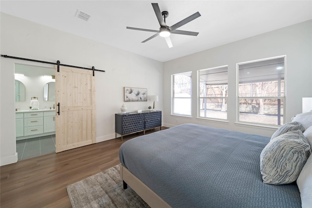 bedroom featuring visible vents, a barn door, connected bathroom, wood finished floors, and baseboards