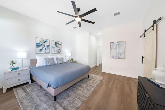 bedroom featuring wood finished floors, visible vents, baseboards, and a barn door