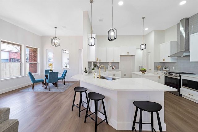 kitchen featuring a breakfast bar area, stainless steel gas stove, a sink, wood finished floors, and wall chimney exhaust hood