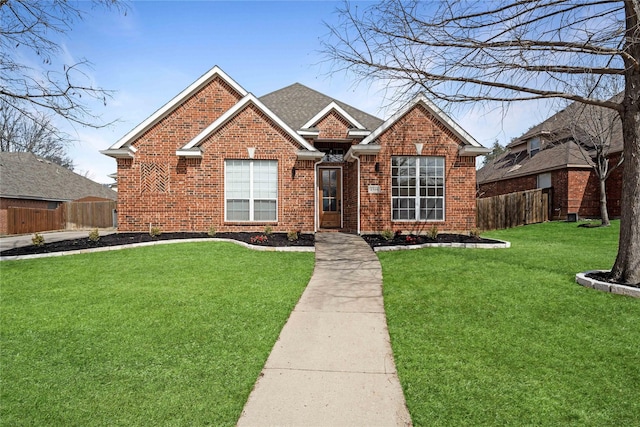 view of front of home with a shingled roof, a front yard, fence, and brick siding