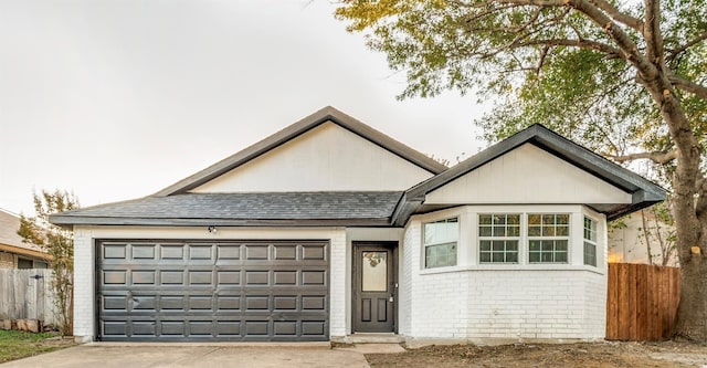 ranch-style house with a shingled roof, concrete driveway, an attached garage, fence, and brick siding