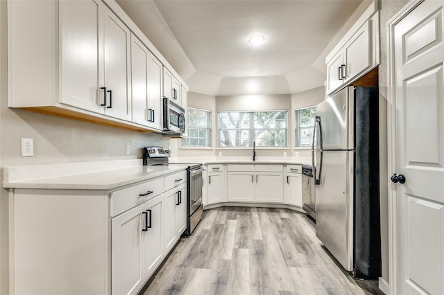 kitchen with a sink, white cabinetry, light wood-style floors, appliances with stainless steel finishes, and a raised ceiling