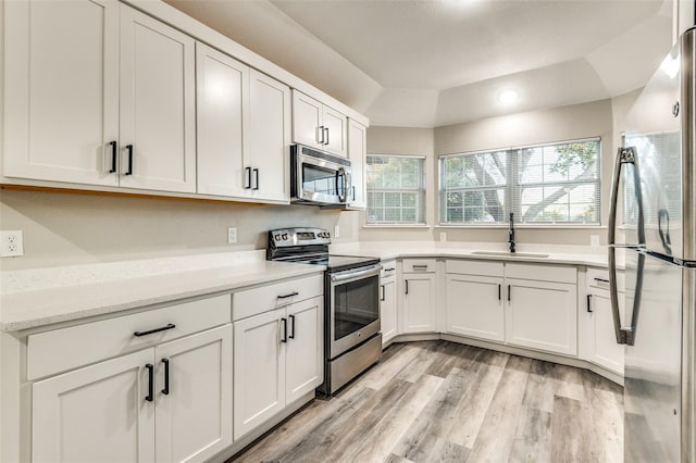 kitchen with light wood finished floors, appliances with stainless steel finishes, a sink, and white cabinetry