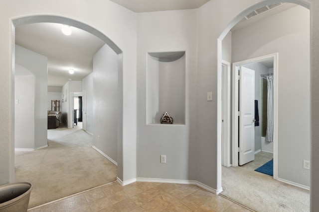 hallway with baseboards, visible vents, arched walkways, and carpet flooring