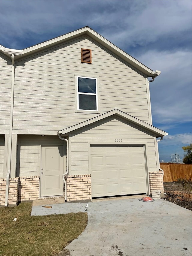 view of front of property featuring a garage, driveway, brick siding, and fence