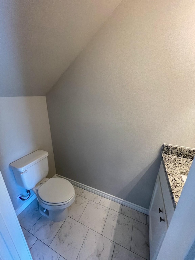 half bathroom with toilet, marble finish floor, baseboards, and vaulted ceiling