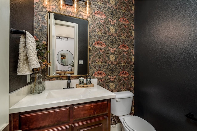 half bathroom featuring vanity, toilet, and wallpapered walls