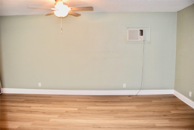 empty room featuring a textured ceiling, a ceiling fan, baseboards, light wood-style floors, and a wall mounted air conditioner