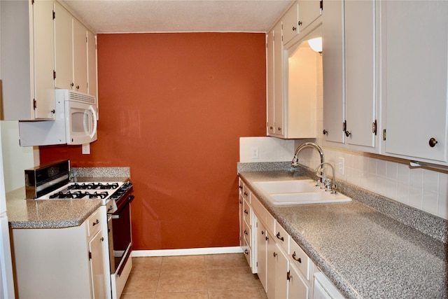 kitchen featuring range with gas stovetop, white microwave, white cabinetry, a sink, and baseboards