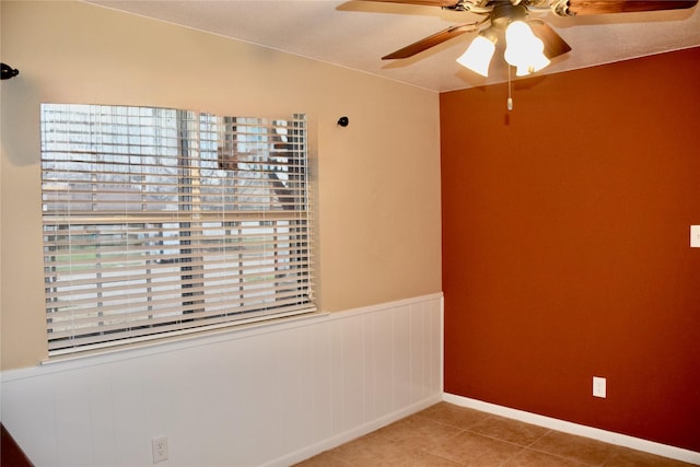 empty room featuring a wainscoted wall, ceiling fan, and tile patterned floors