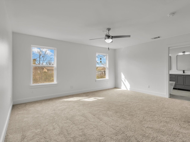 carpeted spare room featuring a sink, baseboards, visible vents, and a ceiling fan