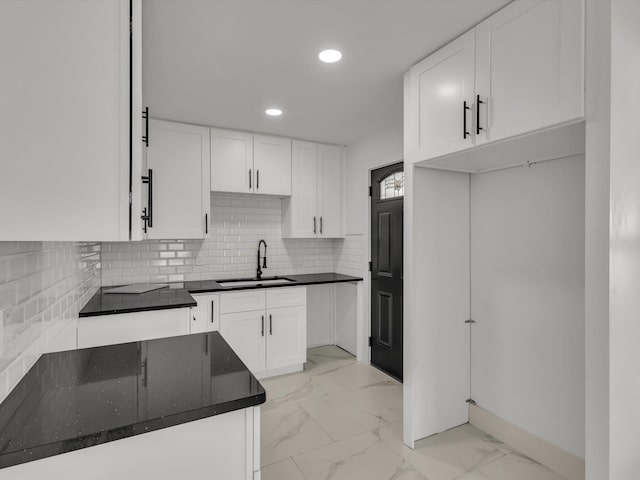 kitchen featuring recessed lighting, a sink, marble finish floor, backsplash, and dark stone counters