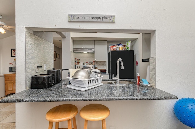 kitchen with a kitchen breakfast bar, dark stone countertops, freestanding refrigerator, a peninsula, and a sink