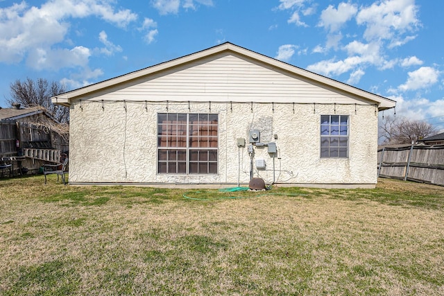 rear view of house with a yard, fence, and stucco siding