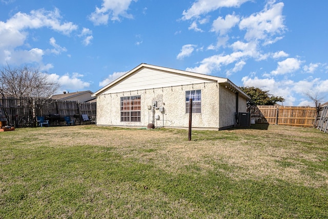 rear view of house featuring a yard, central AC unit, a fenced backyard, and stucco siding