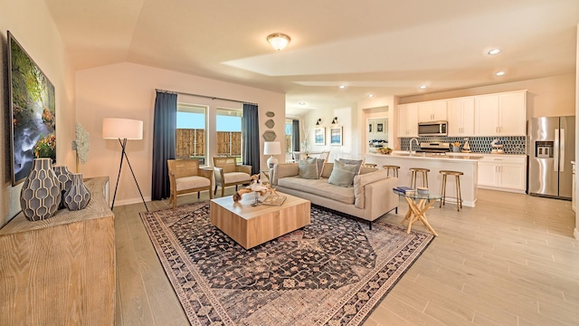 living room featuring light wood-style floors, lofted ceiling, baseboards, and recessed lighting